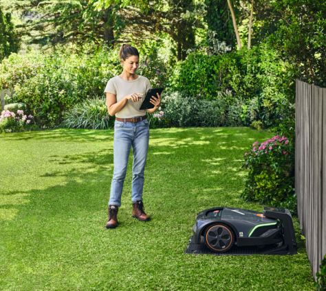 Frau im Garten mit Tablet steuert STIHL iMow EVO Mähroboter