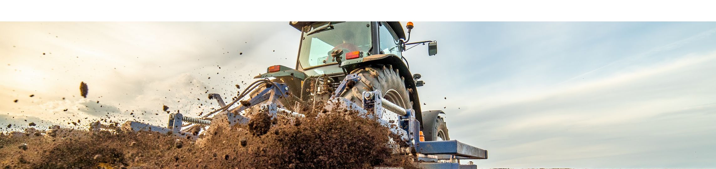 Ein Traktor bearbeitet ein Feld – während der Boden umgepflügt wird, wirbelt die Maschine dunkle, lockere Erde auf. Im Hintergrund erstreckt sich die Ackerfläche bis zum Horizont.