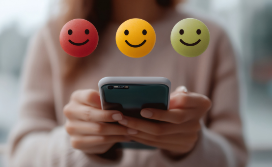 Illustration mit drei Smiley-Symbolen in Rot, Gelb und Grün für eine Umfrage-Bewertung; darunter Hände, die ein Smartphone halten,