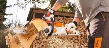 Ein Mann sägt draußen ein Stück Holz mit einer STIHL Kettensäge.