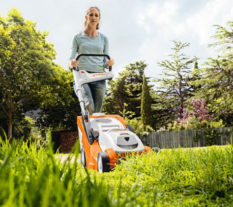 Frau mäht den Rasen mit einem STIHL Rasenmäher – Frontansicht beim Mähen in einem gepflegten Garten.