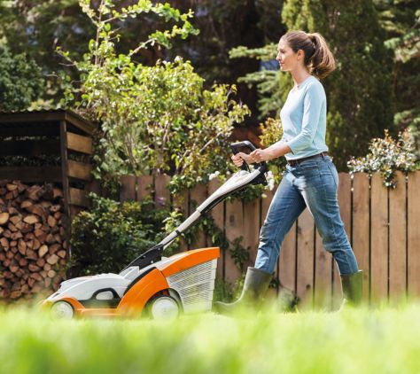 Frau mäht den Rasen mit einem STIHL Rasenmäher – Seitenansicht beim Mähen in einem sonnigen Garten.