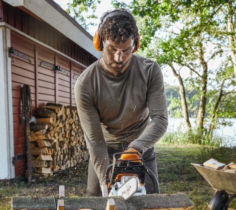 Mann sägt mit STIHL Kettensäge Holz und trägt dabei Schutzbrille und Handschuhe.