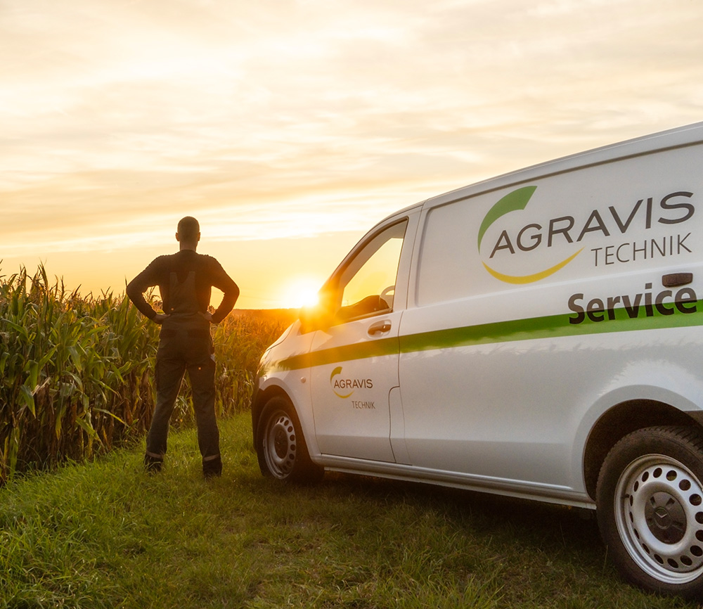 Ein AGRAVIS Mitarbeiter steht neben einem Servicewagen und blickt auf ein Maisfeld – Symbol für Kundennähe und landwirtschaftliche Verbundenheit.